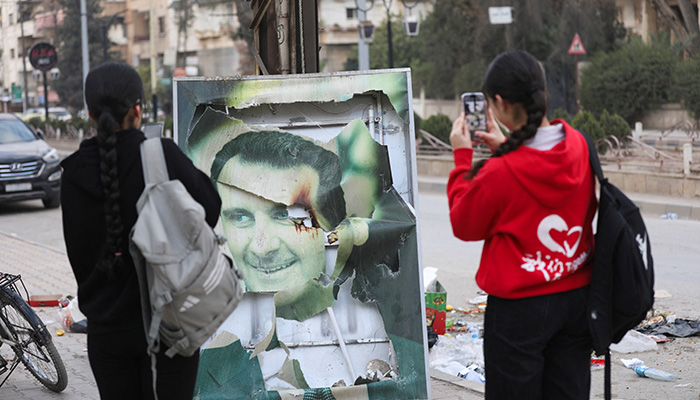 Women use their mobile phones near a damaged picture of Syrian President Bashar al-Assad as people celebrate, after Syrian rebels announced that they have ousted President Bashar al-Assad, in Qamishli, Syria December 8, 2024. — Reuters