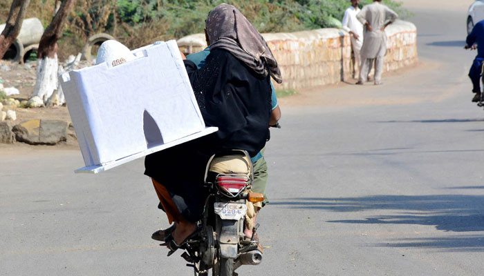 A woman carrying replica model of Quaid-e-Azam tomb while sitting on the rear seat of a motorcycle on the way at Alamgir Road in Lahore on November 15, 2024. — APP.