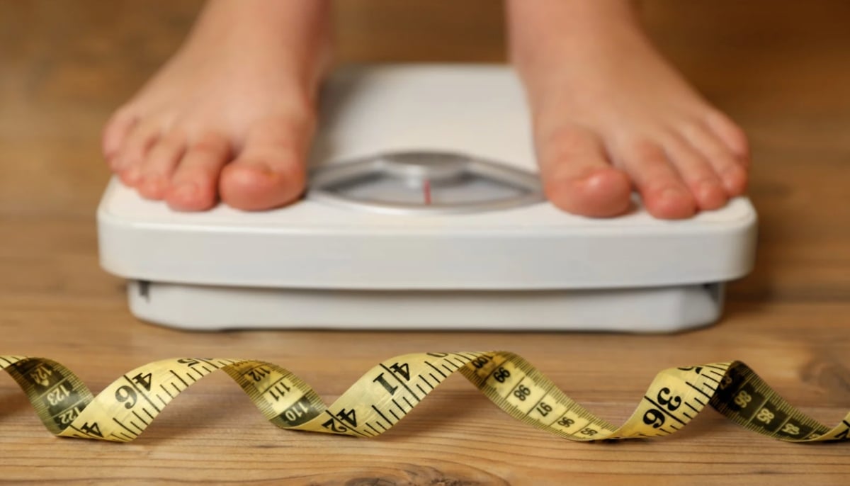 A representational image of a woman standing on a weighing scale. — Canva