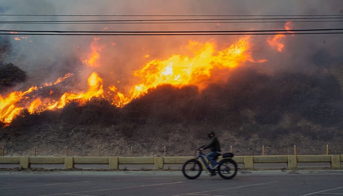 A person rides a bike as the Palisades fire burns during a weather driven windstorm on the west side of Los Angeles, California, US on January 7, 2025. — Reuters