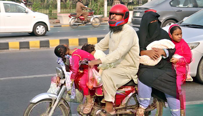 A family is traveling on an overloaded motorcycle, posing a potential risk to their lives, on Mall Road in Lahore on Tuesday, December 3, 2024. — PPI
