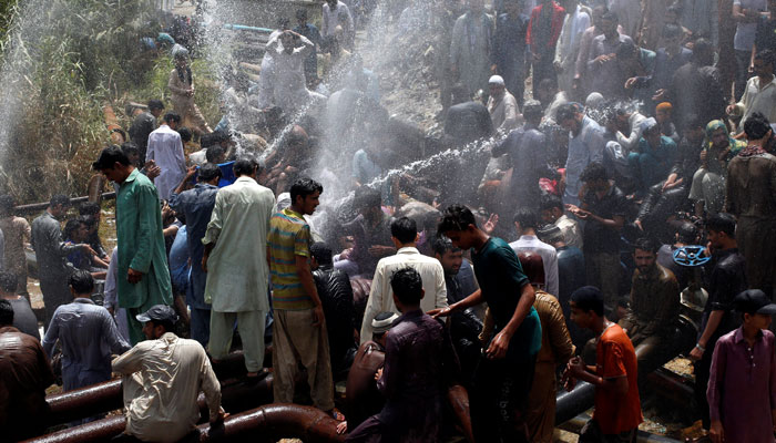 Residents cool off from the heatwave, as they are sprayed with water jetting out from a leaking water pipeline in Karachi. — Reuters/File