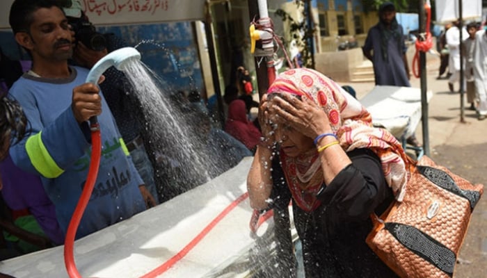 A volunteer showers a woman with water during a heatwave in Karachi. — AFP/File