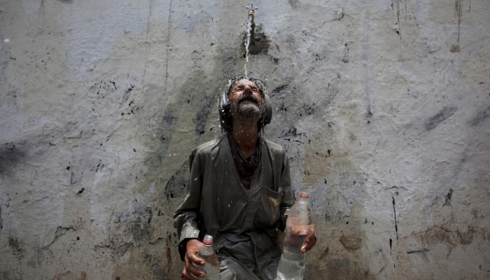 A man cools off from a public tap after filling bottles during intense hot weather in Karachi. — Reuters