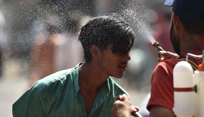 An Edhi volunteer sprays water on a person along a street during a hot summer day in Karachi on May 30, 2024. — INP