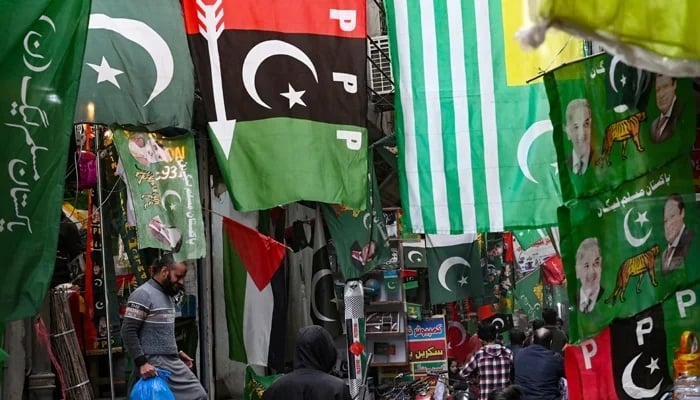 People walk past flags of political parties displayed for sale at a market in Lahore on January 13, 2024. — AFP