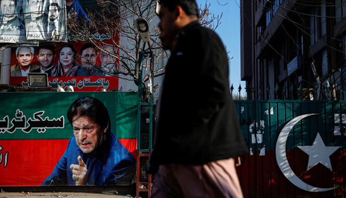 People walk past a banner with a picture of PTI founder Imran Khan outside the party office in Lahore on February 9, 2024. — Reuters
