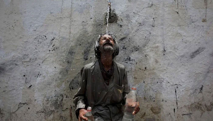 A man cools off from a public tap after filling bottles during intense hot weather in Karachi. — Reuters/File