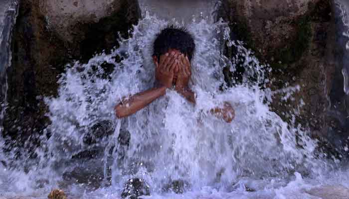 A boy cools off under a water pipe from a canal during a hot summer day. — Reuters/File