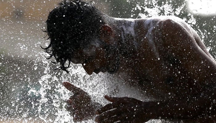 A man cools off at a punctured water supply line on a road as heatwave continues in Karachi. — INP/File