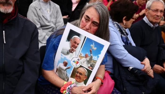 A faithful holds a placard with images of Pope Francis ahead of a rosary, following the death of the pontiff, in St. Peters square, at the Vatican, April 21, 2025. — Reuters