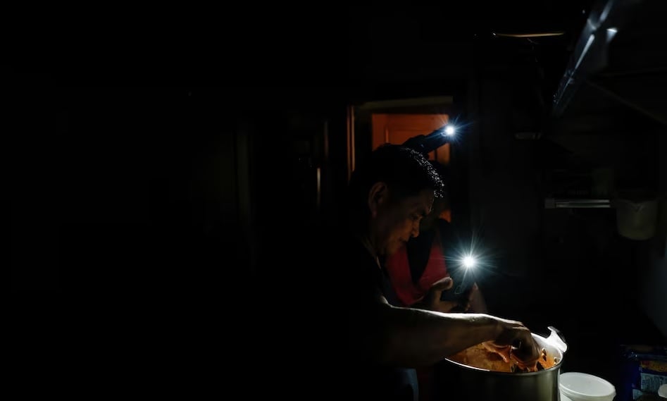 A cook at a takeout restaurant works in a dark kitchen with the aid of phone flashlights during a power outage in Madrid. — Reuters