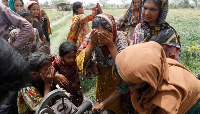 Women and children wash themselves using a hand pump, after work at a muskmelon farm on the outskirts of Jacobabad, May 17, 2022. — Reuters