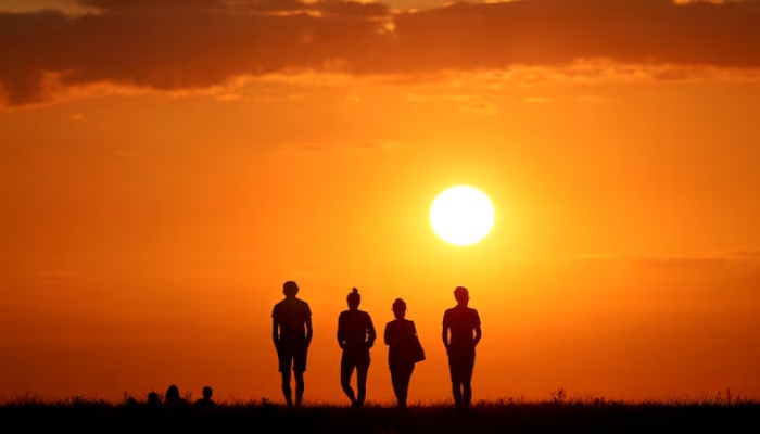 People are silhouetted against the setting sun on top of the Drachenberg in Berlin, Germany, on August 19, 2019. — Reuters