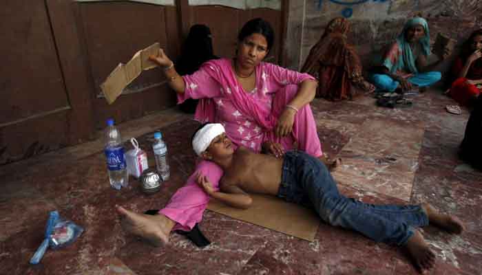 A woman uses a piece of cardboard to fan her son, while waiting for their turn for a medical checkup, outside Jinnah Postgraduate Medical Centre during intense hot weather in Karachi. — Reuters/File