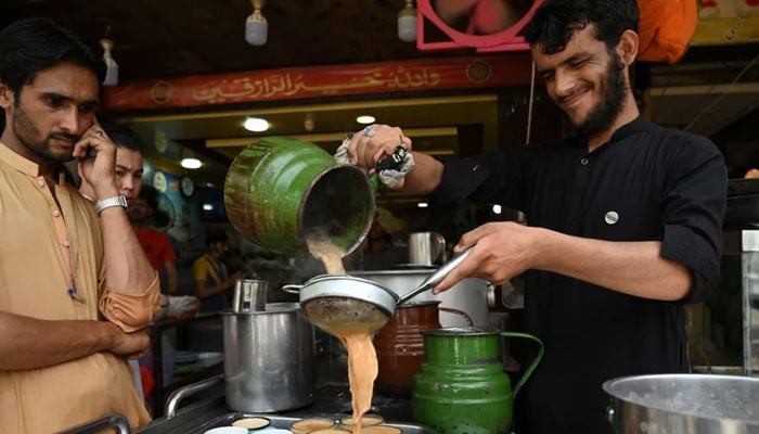 A worker pours cups of tea for customers at a tea shop. — AFP/File