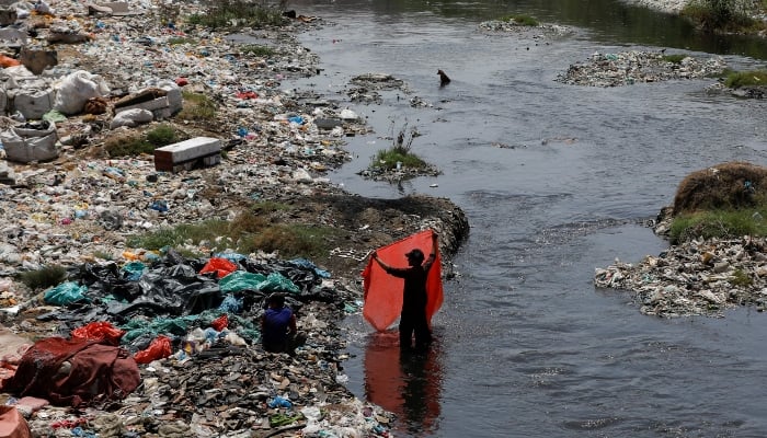 A man washes waste plastic sheets, collected for recycling, in the polluted waters on World Environment Day in Karachi, June 5, 2023. — Reuters