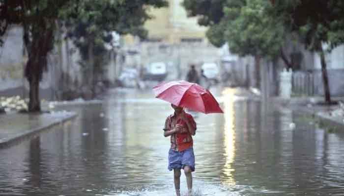 A child wearing an umbrella walks in rainwater on a street. - Reuters / File