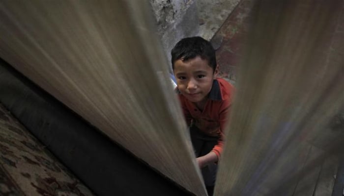 A boy is photographed as he weaves carpets at a workshop on the outskirts of Peshawar. — Reuters/File