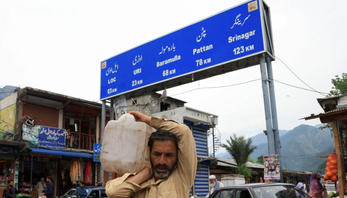 A man carries a jerrycan on his shoulder with the signboard in the background in Chakothi Village on the Line of Control (LoC) in Azad Kashmir on May 2, 2025. — Reuters