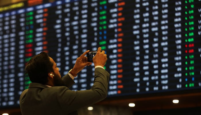 A man uses a mobile phone as he takes a photo of the electronic board displaying share prices during a trading session at the Pakistan Stock Exchange, in Karachi, November 28, 2023. — Reuters