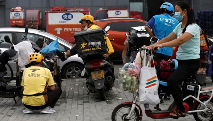 A woman rides an electric bicycle with her groceries past delivery workers of Meituan and Ele.me in Beijing, China July 13, 2020. — Reuters