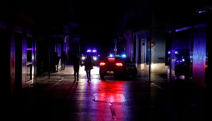 People walk along a shopping street without electric lighting as police cars patrol to prevent theft and looting in the stores during a power outage which hit large parts of Spain, in Ronda, Spain April 28, 2025 — Reuters