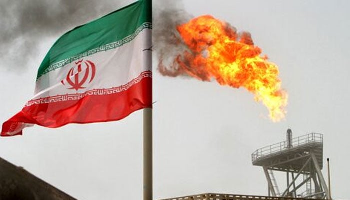 A gas flare on an oil production platform in the Soroush oil fields is seen alongside an Iranian flag in the Gulf July 25, 2005. — Reuters