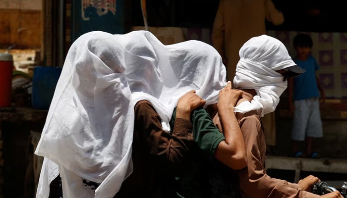 Men ride on a motorbike as they cover their heads with a wet cloth to cool off and to avoid sunlight, during a hot summer day, as the heatwave continues in Jacobabad, on May 26. — Reuters