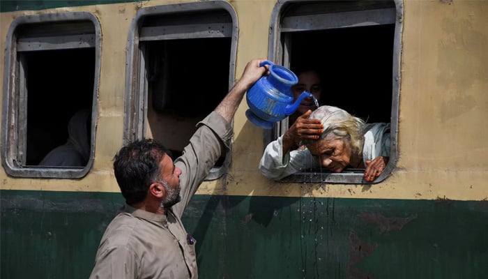 A woman, leaning out of a train window, receives water on her head to cool off during a hot and humid day at the Hyderabad Railway Station in Hyderabad. — Reuters
