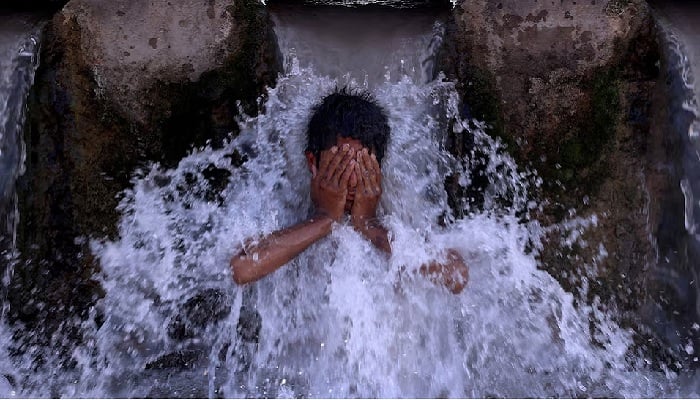 A boy cools off under a water pipe from a canal during a hot summer day on the outskirts of Peshawar, Pakistan, May 28, 2024.— Reuters