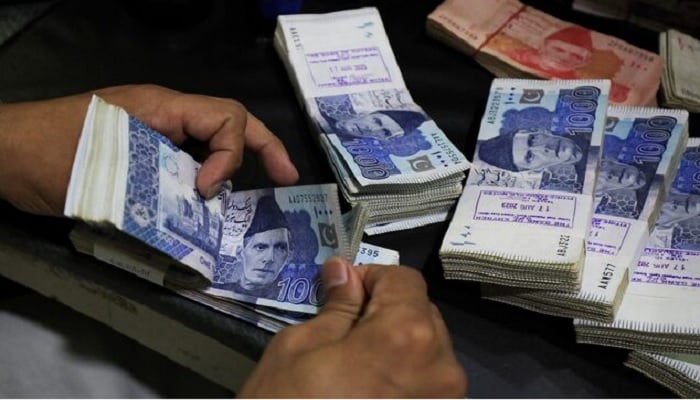 An employee counts Pakistani rupee notes at a bank in Peshawar. — Reuters