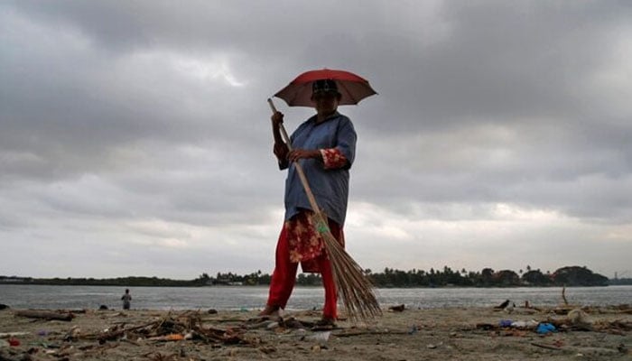 A worker cleans a beach, against the backdrop of pre-monsoon clouds, at Fort Kochi beach in Kochi, May 9, 2019 — Reuters