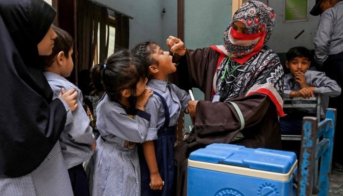 A health worker administers polio drops to school children for vaccination during a door-to-door poliovirus eradication campaign in Lahore on April 21, 2025. — AFP
