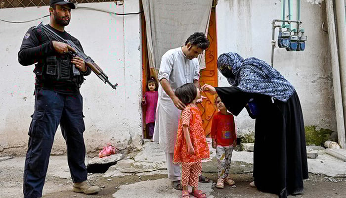 A cop (left) standing guard as a health worker (right) administers polio drops to a child during a door-to-door poliovirus vaccination campaign on the outskirts of Peshawar on October 29, 2024. — AFP