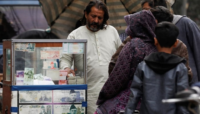 A currency broker stands near his booth, which is decorated with pictures of currency notes, while dealing with customers, along a road in Karachi.— Reuters/File