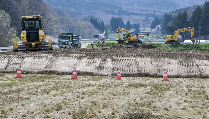 This photo taken on April 22, 2025, shows workers adding clean top soil to a rice field in the village of Iitate, Fukushima prefecture. — AFP
