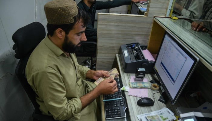 A bank staff counts Afghan currency notes as Taliban government employees wait to receive their salaries at the New Kabul Bank in Kandahar on June 2, 2025. — AFP