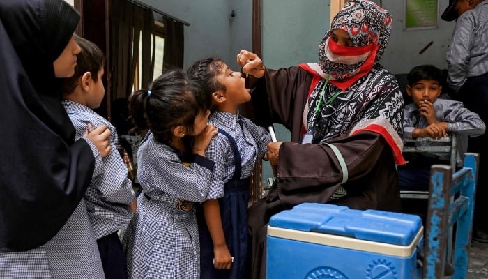 A health worker administers polio drops to school children for vaccination during a door-to-door poliovirus eradication campaign in Lahore on April 21, 2025. — AFP