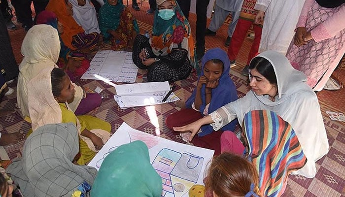 This handout picture taken and released by Chief Minister House Office of Sindh Province on October 12, 2022 shows Nobel Peace laureate Malala Yousafzai (R) speaking with flood-affected children at a makeshift school in Johi, Dadu district of Sindh province. — AFP