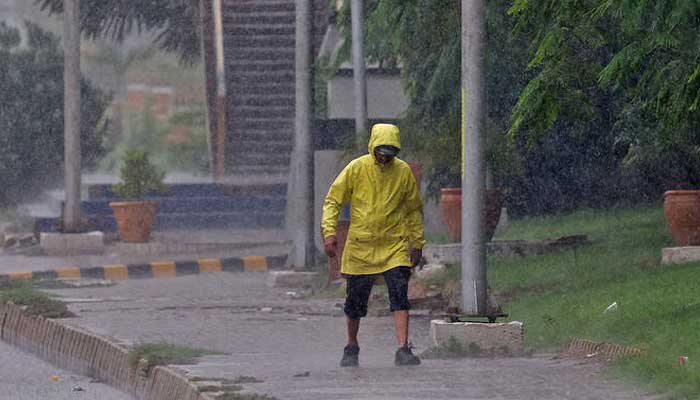 A man wears a rain jacket as he walks along a side walk during a rain in Karachi. — Reuters