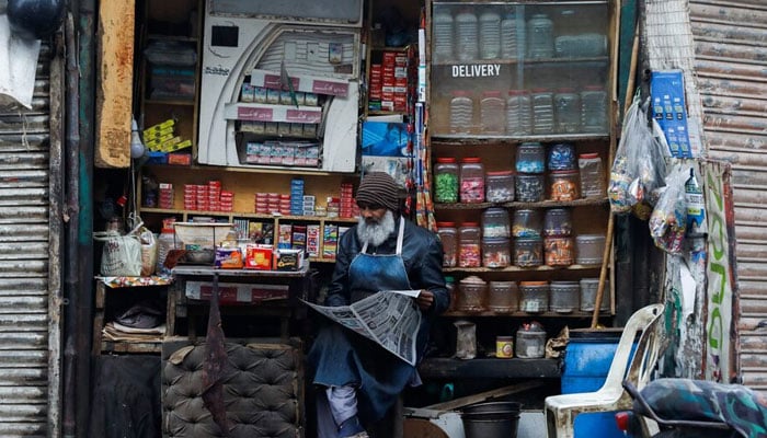 A man reads newspaper while selling betel leaves, cigarettes and candies from a shop in Karachi on December 30, 2021. — Reuters