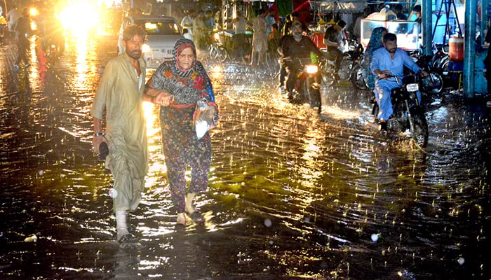 A man helps a woman to walk through the rainwater accumulated on the road during rain in Hyderabad, on June 26, 2025. — APP