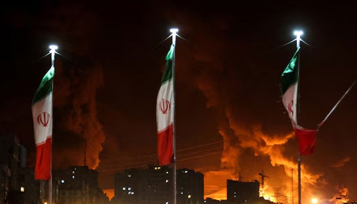 Iranian flags fly as fire and smoke from an Israeli attack on Sharan Oil depot rise, following Israeli strikes on Iran, in Tehran on June 15, 2025. — Reuters