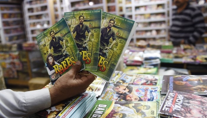 A vendor poses for a photograph with copies of Indian Bollywood film Raees at his shop in Karachi on February 8, 2017. — AFP