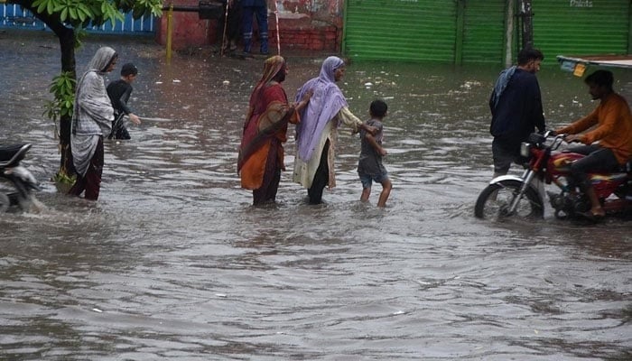 People passing through accumulated water on the road during rain in Lahore. — APP/File