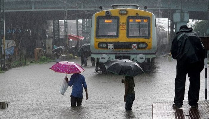People cross inundated railway tracks next to a parked passenger train during heavy monsoon rains in Mumbai, India, June 9, 2021. — Reuters