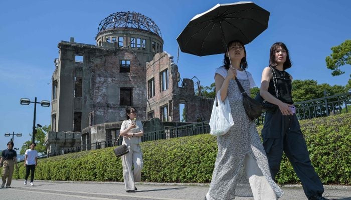 This photo taken on June 28, 2025 shows a woman uses an umbrella to shield herself from the sun among people walking past the Atomic Bomb Dome in the centre of Hiroshima, Hiroshima prefecture, Japan. — AFP