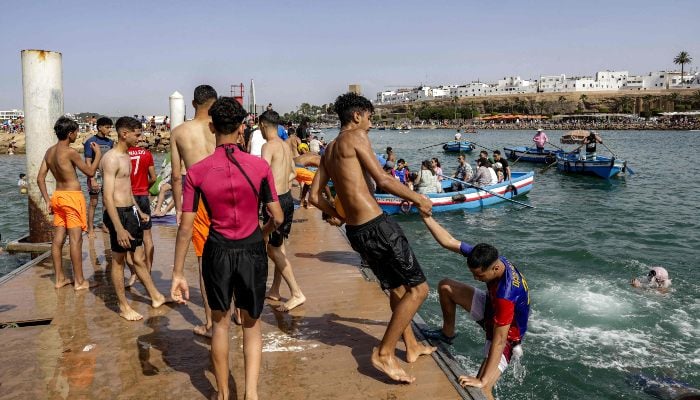 A youth helps another climb from out of the water onto a platform at the beach of Sale during a heatwave in Rabat, Morocco, on June 29, 2025. — AFP