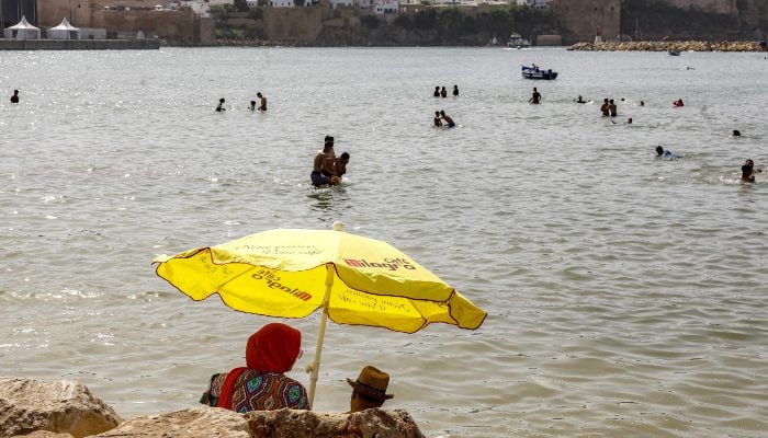 A couple sits under an umbrella at the beach of Sale during a heatwave in Rabat, Morocco, on June 29, 2025. — AFP